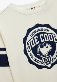 Sudadera blanca con un gran logo circular de color azul marino que dice "JOE COOL" y "50 AÑOS", y un personaje de dibujos animados que lleva gafas de sol.