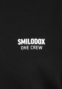 Czarny sweter z okrągłym dekoltem z białym napisem "SMILODOX ONE CREW" nadrukowanym z przodu. Wykonany z gładkiego, elastycznego materiału.