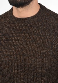 Dunkelbrauner gestrickter Pullover mit einem strukturierten Muster, der einen gerippten Rundhalsausschnitt und eine enganliegende Silhouette aufweist.