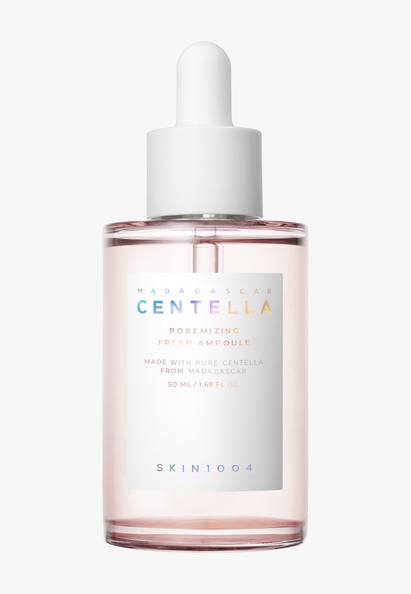 Szklana butelka z różowym odcieniem, zakrętką z pipetą oraz białą etykietą z tekstem w kolorach tęczy. Zawiera 50 ml ampułki zmniejszającej pory.