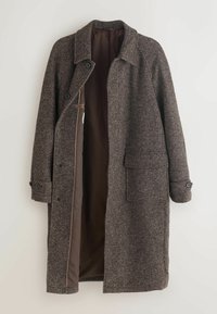 Brun, tekstureret uldfrakke med slagkrave, frontknapper og sidelommer. Fóret indvendigt i en kontrastfarvet brun tone.