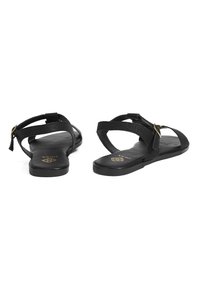 Black sandals with textured straps and a gold buckle accent. The flat sole features a smooth finish, designed for comfort and ease of wear.