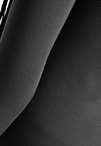 Tessuto nero a righe che mostra linee curve e texture, con aree lisce e tese. Il materiale appare morbido e leggero.