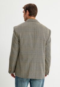 Grau kariertes Blazer mit leicht oversized Passform, braunen und cremefarbenen Akzenten sowie Knöpfen mit vier Knöpfen, aus strukturiertem Stoff.
