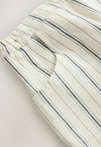 Tissu de couleur crème avec de fines rayures noires, doté d'une taille élastique et de détails cousus. Texture lisse, forme fuselée.