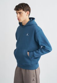 Μπλε φούτερ με κουκούλα και τσέπη καγκουρό, κατασκευασμένο από απαλό ύφασμα. Διαθέτει λευκό κεντητό λογότυπο στο στήθος. Συνδυάζεται με γκρι φόρμα.