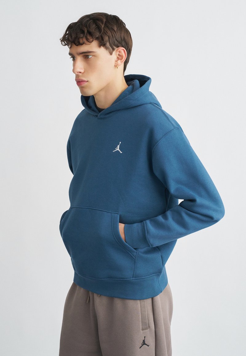 Μπλε φούτερ με κουκούλα και τσέπη καγκουρό, κατασκευασμένο από απαλό ύφασμα. Διαθέτει λευκό κεντητό λογότυπο στο στήθος. Συνδυάζεται με γκρι φόρμα.