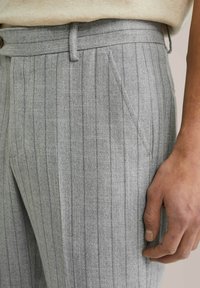 Pelēki vertikāli svītroti bikses, izgatavotas no teksturēta auduma. Tām ir pogu aizdare, sānu kabatas un pielāgota piegriezuma.