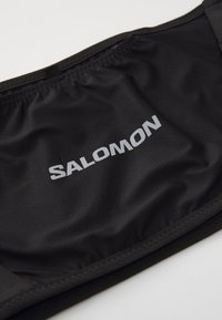 Svart midjebånd med den sølvfargede "SALOMON"-logoen. Laget av teksturert, elastisk materiale med en glatt overflate og elastiske kanter.