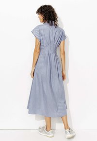Robe à rayures bleues avec de courtes manches courtes, taille cintrée et jupe fluide. Portée avec des baskets argentées, affichant un look décontracté et casual.