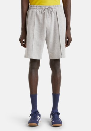 Pantalones cortos deportivos de color gris claro con una cinturilla elástica, que presentan pliegues y bolsillos laterales, llevados con calcetines azul oscuro y zapatillas deportivas.