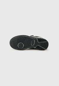 Semelle de chaussure de sport noire avec grip en caoutchouc texturé, accents circulaires et motif de semelle ; comprend une zone de talon renforcée et un design flexible.