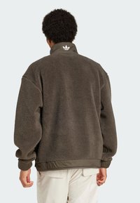 Fleecejacke in Dunkelgrau mit hohem Kragen, gerippten Bündchen und Saum. Mit einem weißen Logo am Kragen und strukturiertem Stoff.