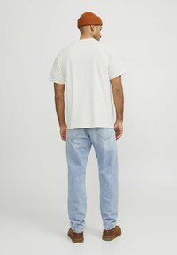 Ljusbeige bomullströja med avslappnad passform, i kombination med ljusblå jeans. Modellen har på sig en orange ribbad mössa och bruna skor.