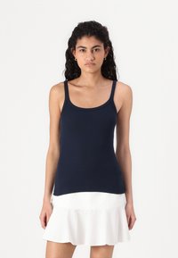 Top sin mangas de color azul marino con tirantes finos y un diseño ajustado, combinado con una falda blanca acampanada que presenta un dobladillo con volantes.