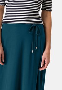 Jupe sarcelle avec taille à cordon décorée d'accents argentés, associée à un haut rayé à manches courtes avec bords festonnés.