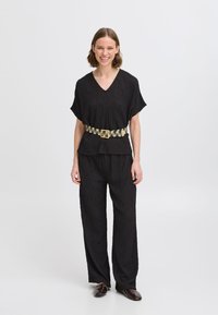 Černý texturovaný outfit se zavinovacím výstřihem a kalhotami širokého střihu, stáhnutý v pase vzorovaným béžovým a černým pásem.