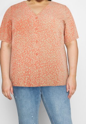 Top a V con bottoni di un beige chiaro con un motivo astratto corallo, maniche corte e vestibilità comoda, abbinato a jeans leggeri blu strappati.