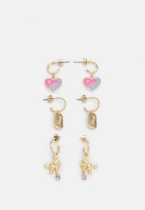 Brincos em tom de ouro com charms em forma de coração nas cores rosa e roxo, etiquetas gravadas e pendentes de ursinho de pelúcia com detalhes roxos.