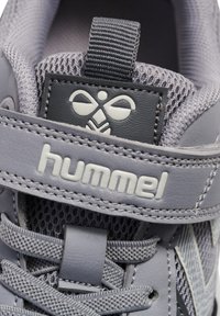 Grå sportssko med mesh-overdel og syntetiske overlays. Har velcrorem, snørebånd og branding på en tekstureret lap.