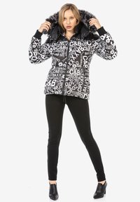 Pufferjacke in zwart en wit met grafische print, voorzien van een nep-bont gevoerde capuchon, rits sluiting en geribbelde manchetten. Zwarte aansluitende broek en schoenen.