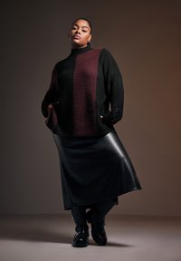 Oversized svart och vinröd stickad tröja med texturerad yta, matchad med en svart fusk läderkjol och svarta knähöga stövlar.