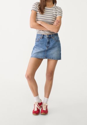 Denim skirt in light blue, A-line shape, mid-thigh length, with subtle fading. Paired with a striped short-sleeve top and red sneakers.