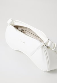 Sac à main en cuir blanc avec une texture lisse, une forme incurvée, une fermeture éclair et une bandoulière ajustable. Présente un design minimaliste et un branding discret.