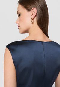 Námořnické saténové šaty s elegantním designem krátkého rukávu, které mají nenápadný zadní zip a hladkou texturu, prezentované zezadu.