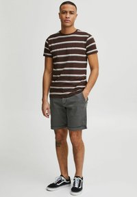T-shirt à manches courtes rayé marron et blanc, associé à un short gris. Modèle portant des baskets noires et blanches. Design simple et décontracté.