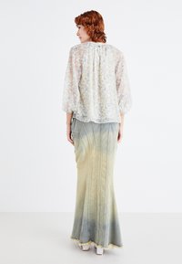 Blusa trasparente a fantasia floreale con maniche a sbuffo abbinata a una lunga gonna di denim con sfumature, caratterizzata da orlo sfilacciato e cuciture verticali.