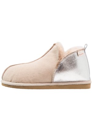 Beige semsket slipper med en metallisk sølvdetalj. Myk innvendig fôr, avrundet tå og en teksturert gummisåle for godt grep.