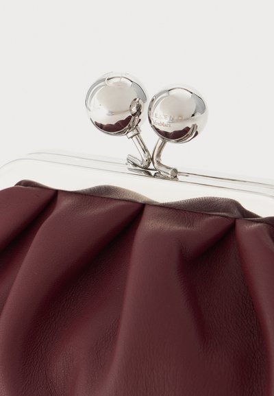 Gros plan d'un sac à main en cuir bordeaux avec une fermeture argentée brillante comportant deux boutons sphériques et un marquage gravé.