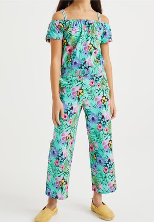 Tropisk off-shoulder top og bukser med vid ben i mintgrøn, med farverige blomsterprint og elastisk talje. Sat sammen med gule sko.