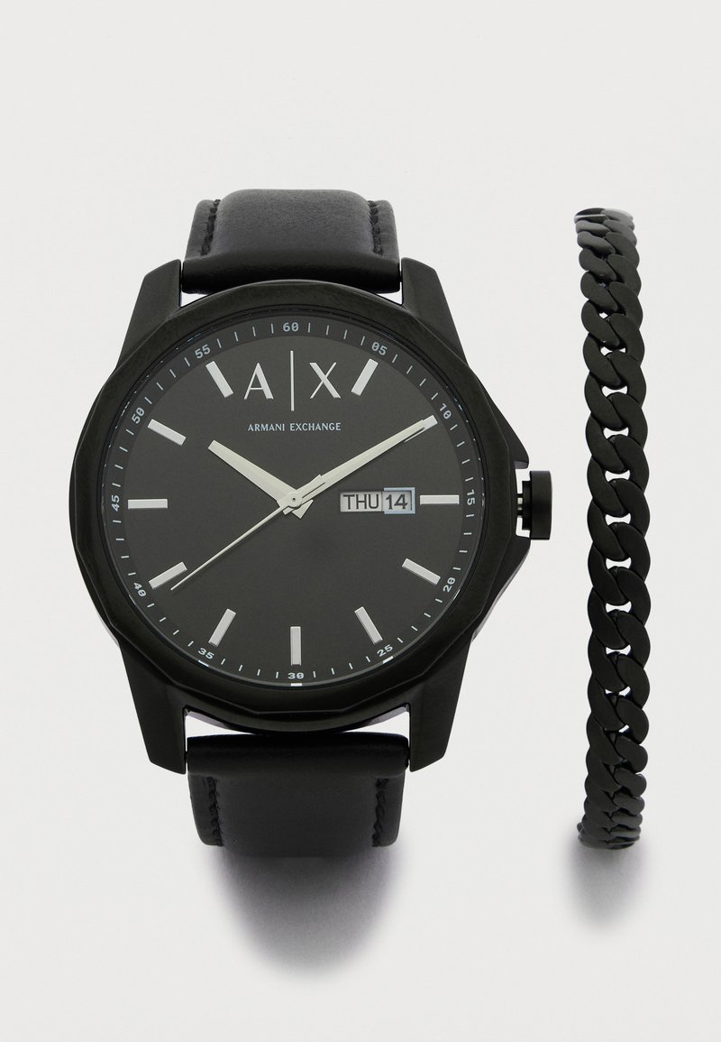 Črna silikonska ura z okroglo številčnico, belimi oznakami ur, prikazom datuma in črnim usnjenim pasom. Vključuje črno verižico.