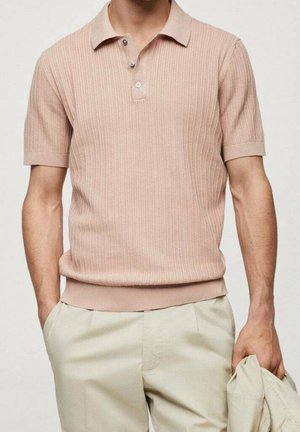 Polo rose clair à manches courtes avec texture côtelée, col à trois boutons et ceinture contrastante. Porté avec un pantalon de couleur claire.