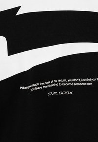 Tissu noir avec une grande flèche blanche et texte blanc : « Quand vous atteignez le point de non-retour, vous ne trouvez pas seulement votre vie… » Logo SMILODOX en dessous.