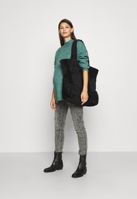 Geantă de umăr din corduroy negru cu un design matlasat, asortată cu un pulover teal, blugi gri și cizme negre până la gleznă. Estetică simplă și modernă.