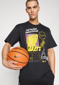 Černé grafické tričko s žlutým a fialovým designem basketbalu, textem a logem Nike. Drží oranžový basketbal s černými akcenty.