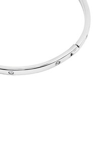 Srebrna metalowa bransoletka o gładkim wzorze, z małymi przezroczystymi kamieniami osadzonymi na powierzchni. Widoczny szczegół zapięcia zapewniający bezpieczeństwo.