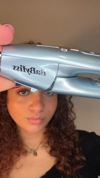 Sølv hårrettetang med elegant design, med en merkevareetikett og ergonomisk grep. Overflaten har en blank finish og subtilt buede kanter.