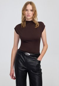 Maglione a collo alto marrone aderente con maniche a cappuccio, abbinato a pantaloni in pelle nera a vita alta con una fibbia in tono argento.