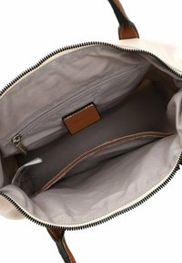 Sac à main beige avec fermeture éclair, doté d'un intérieur lisse, d'une poche zippée, d'une étiquette en cuir marron et d'accents marron.