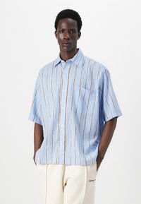 Camisa de botón de manga corta en tela azul claro con rayas verticales marrones, que cuenta con un bolsillo en el pecho y un diseño de cuello clásico.