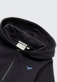 Felpa nera con zip, realizzata in cotone biologico, con un piccolo emblema di un dinosauro blu sul petto, caratterizzata da una morbida texture del tessuto e cappuccio.