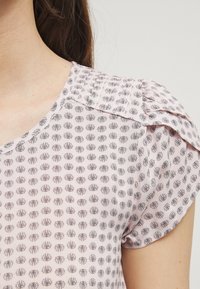 Blusa rosa con un sutil patrón floral en gris oscuro, mangas cortas y un escote redondeado con un ligero fruncido en los hombros.