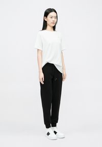 Biele tričko s krátkym rukávom, čierne tepláky so šnúrkou a biele tenisky s čiernymi detailmi. Jednoduchý, voľný strih, hladký povrch.