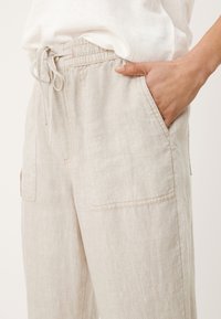 Beiga linbyxor med elastisk midja och dragsko, två sidofickor och en avslappnad passform. Subtil struktur synlig på tyget.