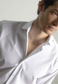 Camisa blanca de vestir con finas rayas verticales, que presenta un collar puntiagudo y detalle de botones, exhibida en una persona con una ligera inclinación.