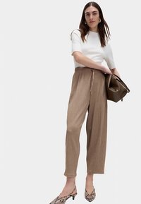 White ribbed short-sleeve top, brown textured wide-leg pants with drawstring, and pointed toe snake-print heels. Holding a brown handbag.